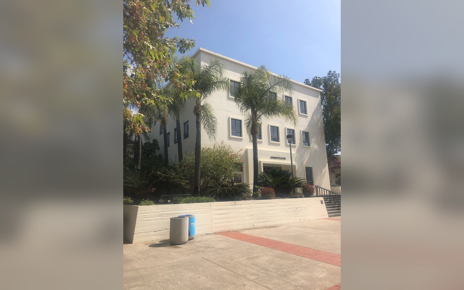 Palm trees line the entrance to a white multi-story administration building
